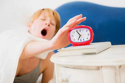 Photo of a sleepy woman reaching for her alarm clock