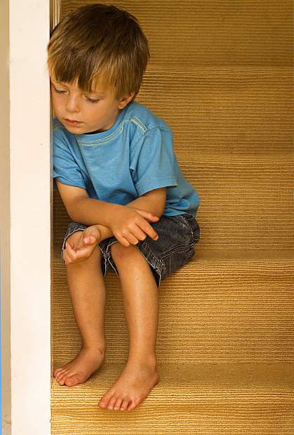 a photo of a young boy, looking down, seated on some stairs