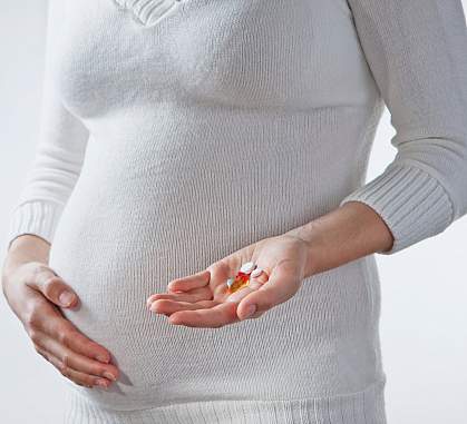 Photo of a pregnant woman holding vitamins in front of her belly