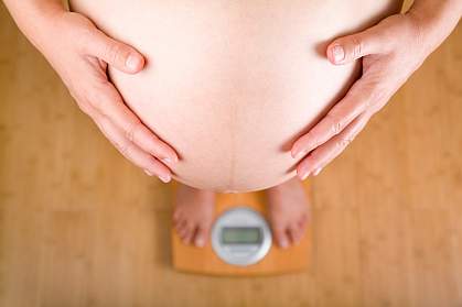 Photo of a pregnant woman on a scale holding her belly
