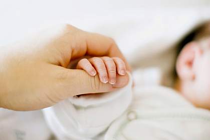 Photo of a newborn's fingertips held by an adult’s hand