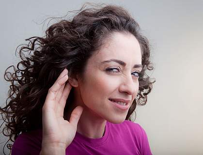 Photo of a young woman cupping her hand to her ear