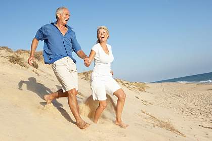 An older couple running down a sand dune.