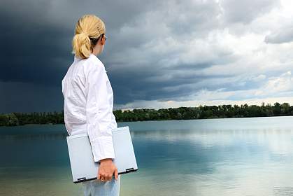 Woman with a laptop looking over a lake as a heavy storm approaches.