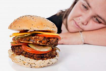 Photo of an overweight young woman resting her head on her arm and gazing longingly at a forbidden cheeseburger.