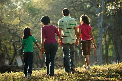 Rückansicht einer Familie, die gemeinsam in einem Park spazieren geht.