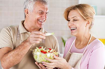 Happy senior couple eating salad in the kitchen.