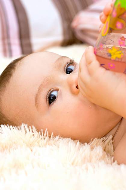 Infant watching someone while drinking from a bottle.