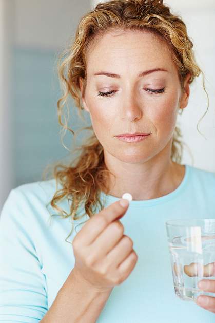 Woman looking pensively at a white pill.
