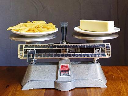 A balance scale with pasta/carbs weighed against butter/fat.