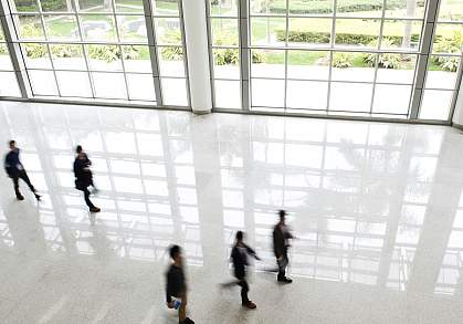 Office workers walking in front of large windows with a view of outdoor gardens.
