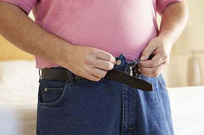Overweight man buttoning his jeans.