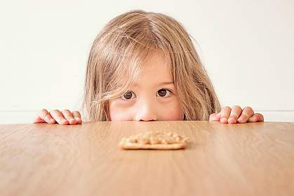 Young girl staring a peanut butter cracker on the table