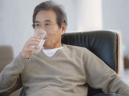Senior man in an armchair drinking a glass of water