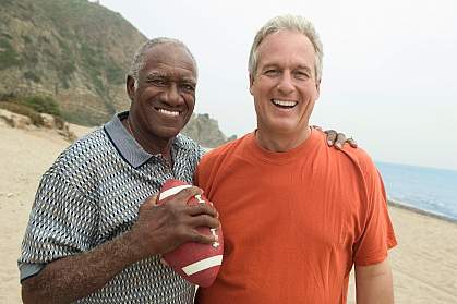 Older men, one black and one white, with a football on the beach