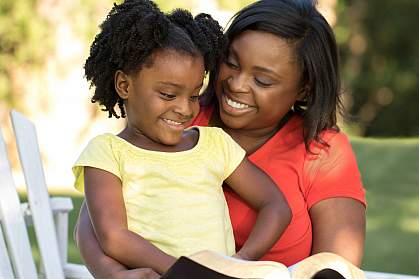 African-American mother and daughter reading outdoors.
