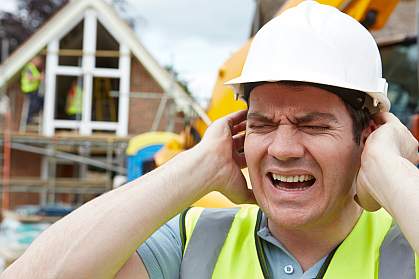 Construction worker holding ears on building site