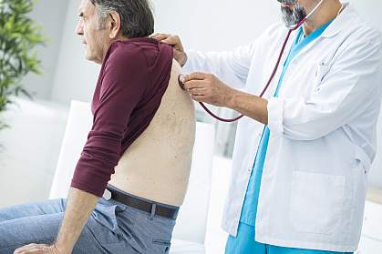 Doctor listening to older man’s lungs.