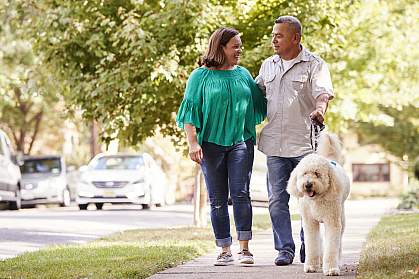 Senior couple walking dog along suburban street