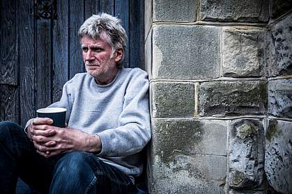 Concerned-looking man leaning on a wall and drinking a beverage