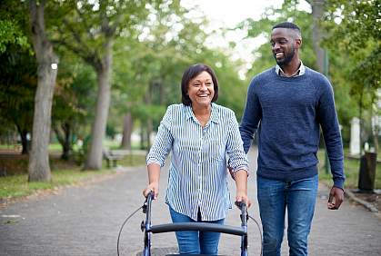 Mature woman using a walker while a young man assists her in the park