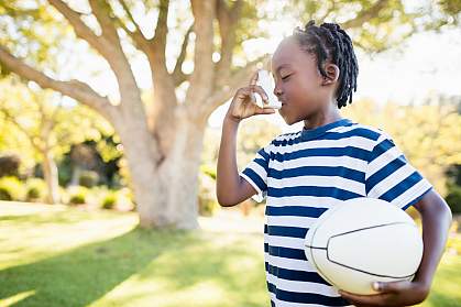 Young child using an inhaler and holding a ball