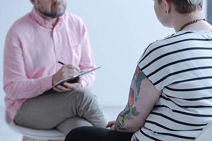 Therapist taking notes while listening to a tattooed young person