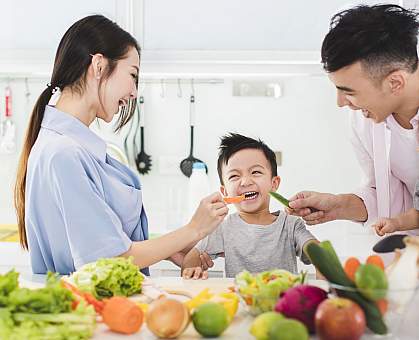 Parents with young boy eating vegetables in the kitchen