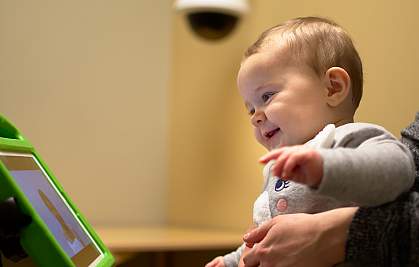 Smiling toddler looking at person on tablet screen