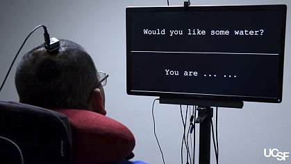 Rear view of man with an electrode array in his head watching a screen with words.