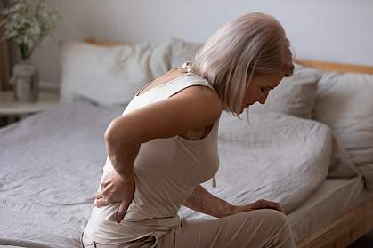 Mature woman sitting in bed holding her lower back