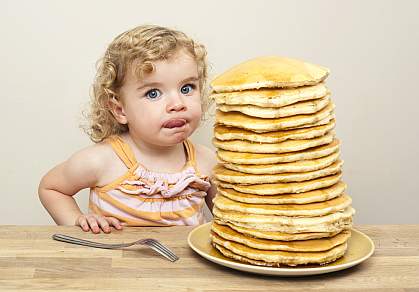 Young girl licking her lips and eying a huge stack of pancakes