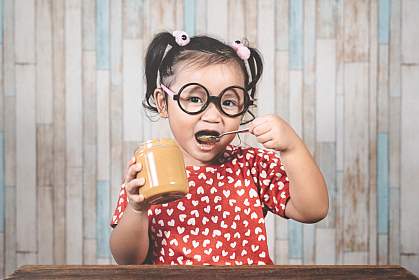 Young Asian girl holding a jar of peanut butter and putting a spoon in her mouth