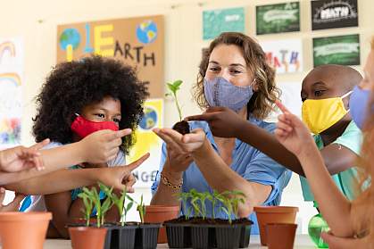 Teacher and students in a classroom wearing masks and looking at seedlings