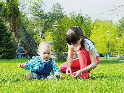Infant boy and older sister playing in the grass