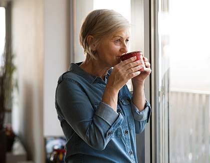 Senior woman looking out a window sipping a cup of tea