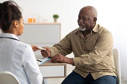 Black female doctor giving an elderly male patient pills