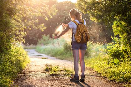 Woman applying insect repellent as mosquitoes fly around her