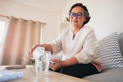 Senior woman pouring water into a glass to drink