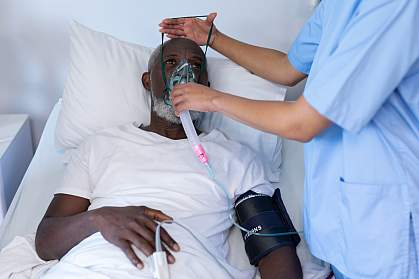Medical worker putting oxygen mask on a senior Black man in a hospital bed 