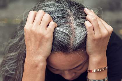 Top view of woman holding gray hair with both hands.