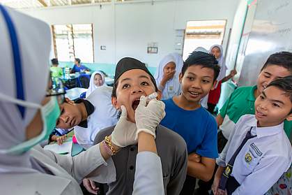 Nurse in a classroom setting giving smiling children an oral vaccine.