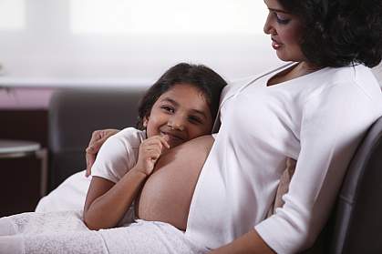 Young girl with her ear against a woman’s pregnant belly