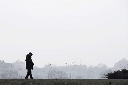 Silhouette of elderly man walking alone outside a city on a hazy, polluted day.