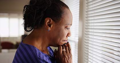 An older black woman mournfully looks out a window.