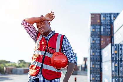 Black male engineer in uniform on a sunny day holding a hard hat and wiping sweat from his brown.