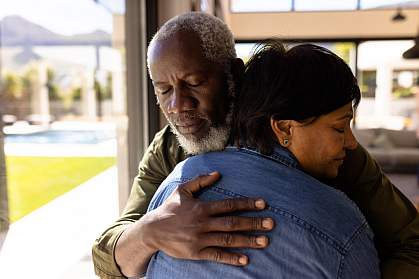 Senior man with his eyes closed embracing a woman while standing in nursing home.