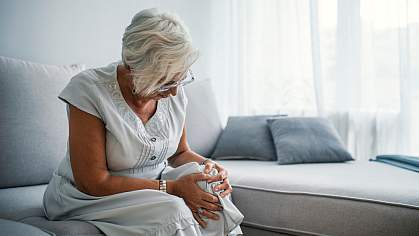 Senior woman on a couch holding her knee in pain.