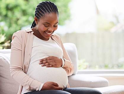 Pregnant woman on sofa smiling down at her belly.