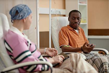 A black man and a white woman with a head scarf talking during chemotherapy treatment in clinic. A black man and a white woman with a head scarf talking during chemotherapy treatment in clinic.